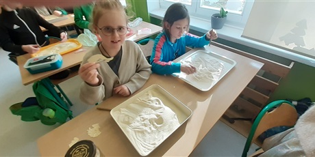 Powiększ grafikę: Zabawa w paleontologa - dziewczynki z 1c szukają elementów papierowego szkieletu dinozaura w kaszy mannej, imitującej piasek.