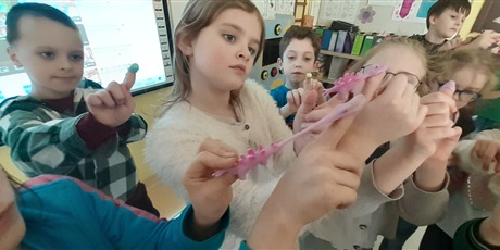 Powiększ grafikę: Dzieci z 1c nakładają na palec procę w kształcie gumowego, rozciągającego się dinozaura.
