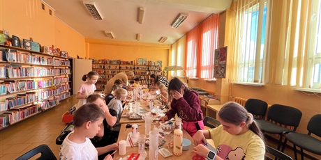 Powiększ grafikę: Dzieci siedzą przy długim stole, wycinają wzory z serwetek, malują klejem.