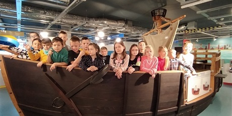 Powiększ grafikę: Dzieci stoją w replice drewnianej łodzi.