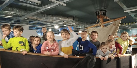 Powiększ grafikę: Dzieci stoją w replice drewnianej łodzi.