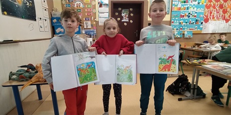 Powiększ grafikę: troje dzieci stoi z zeszytami i pokazują kolorowankę z dinozaurami