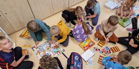 Powiększ grafikę: grupa dzieci siedzi na podłodze i mają rozłożone gry planszowe w które grają