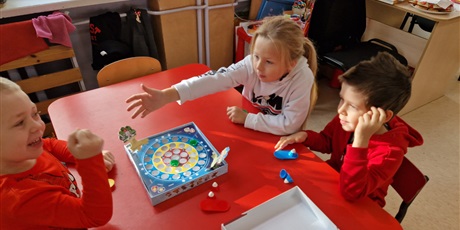 Powiększ grafikę: W sali dwóch chłopców i jedna dziewczyna, siedzą przy stoliku grają w grę.