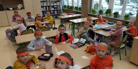 Powiększ grafikę: W ławka siedzą dzieci z pomarańczowymi opaskami na głowach.