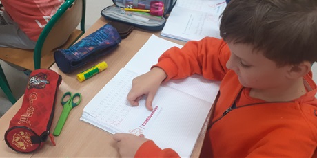 Powiększ grafikę: Chłopiec z klasy 1c wkleja do zeszytu kartkę z napisem "Tumbo pomaga".