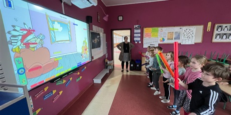 Powiększ grafikę: Dzieci stojąc obserwują wyświetlany obraz, w rękach trzymają rurki do gry.