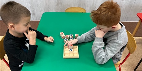 Powiększ grafikę: Dwoje dzieci przy stoliku gra w kółko i krzyżyk.