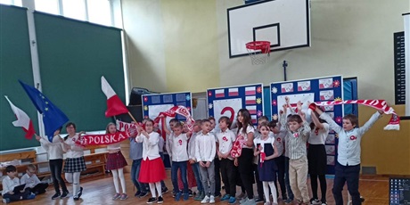 Powiększ grafikę: Grupa dzieci trzyma w rękach flagi Polski i UE oraz szaliki z napisem Polska.