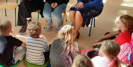 Powiększ grafikę: Grupa dzieci siedzi na podłodze i słucha czytanych tekstów.
