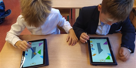 Powiększ grafikę: Dwaj chłopcy siedzą w ławce, rysikiem dotykają ekranu tabletu.