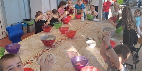 Powiększ grafikę: Dzieci stoją przy stole i mieszają ciasto na pączki.