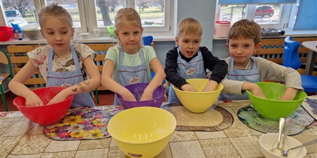Powiększ grafikę: Czworo dzieci ugniata w miskach ciasto na pączki.