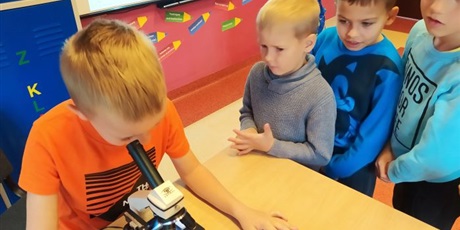 Powiększ grafikę: Chłopiec patrzy przez mikroskop, trzech chłopców patrzy na niego.