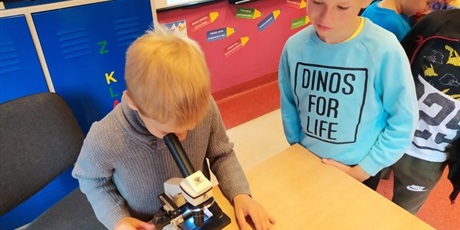Powiększ grafikę: Chłopiec patrzy przez mikroskop, drugi na niego spogląda.
