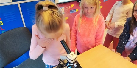 Powiększ grafikę: Dziewczynka patrzy przez mikroskop, trzy pozostałe patrzą na nią.