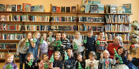 Powiększ grafikę: Grupa dzieci stoi w bibliotece trzymając w rękach wykonane choinki.