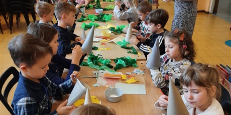 Powiększ grafikę: Przy stole dzieci wykonują papierowe choinki.