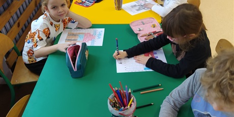 Powiększ grafikę: Przy długim stole dzieci rysują.