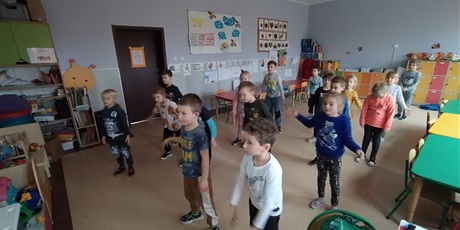 Powiększ grafikę: Dzieci stoją na wolnej przestrzeni i wykonują ruchy rękoma i nogami.