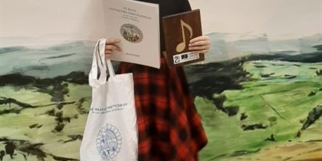 Powiększ grafikę: uczennica stoi z dyplomem i nagrodami za konkurs