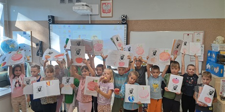 Powiększ grafikę: Dzieci stoją przy tablicy, w rękach trzymają zeszyty. 