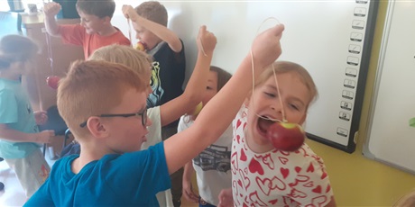 Powiększ grafikę: Dziewczynka próbuje ugryźć jabłko bez użycia rąk trzymane przez chłopca na sznurku.