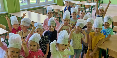 Powiększ grafikę: Dzieci stoją w sali,na głowie mają czapkę kucharza, czekają na zajęcia z kuchcikowania.