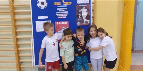 Powiększ grafikę: Drużyna z klasy 1b przed tablicą dotyczącą mistrzostw w piłce nożnej.