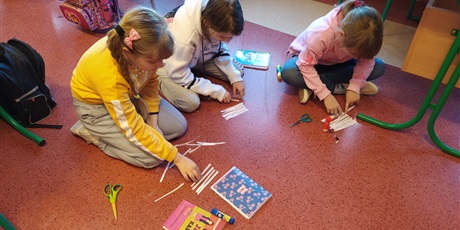 Powiększ grafikę: Trzy dziewczynki siedzą na podłodze i układają karteczki.