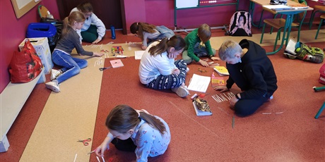 Powiększ grafikę: Na podłodze siedzi 7 dzieci, które czytają i przekładają karteczki.