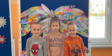 Powiększ grafikę: Troje dzieci stoi na tle kolorowych skrzydeł.