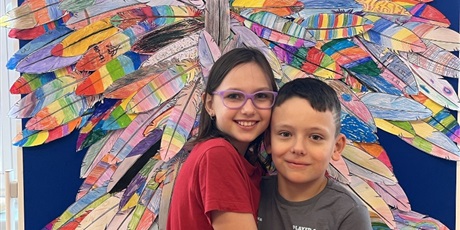 Powiększ grafikę: Dziewczynka z chłopcem stoją na tle kolorowych skrzydeł.