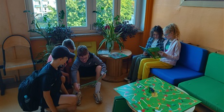 Powiększ grafikę: Grupa uczniów siedzi i czyta książki na szkolnym korytarzu.