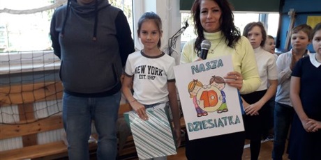 Powiększ grafikę: Uczennica oraz dwóch nauczycieli stoi z nagrodą za konkurs i plakatem "Nasza Dziesiątka".