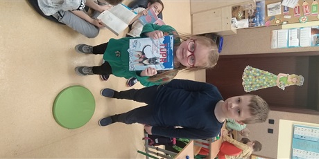 Powiększ grafikę: dziewczynka i chłopiec stoją obok siebie i pokazują książkę