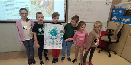 Powiększ grafikę: kilkoro dzieci z 1b stoi obok siebie i trzymają w ręku plakat z planetą Ziemią